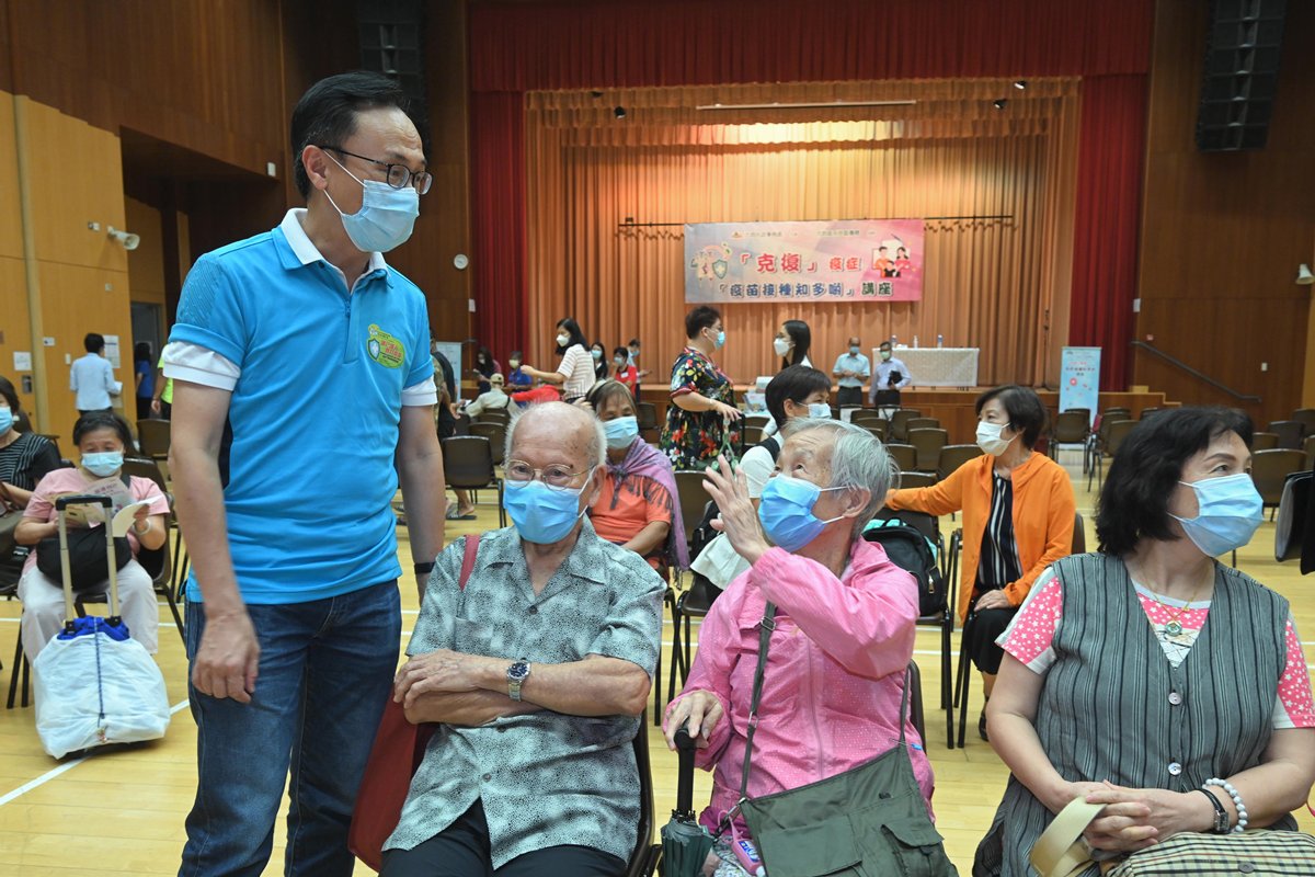 推動接種:  一站式健康講座、醫療諮詢和即時接種新冠疫苗服務移師到天水圍天暉路社區會堂舉行，聶德權（左一）與參加健康講座的長者交談。