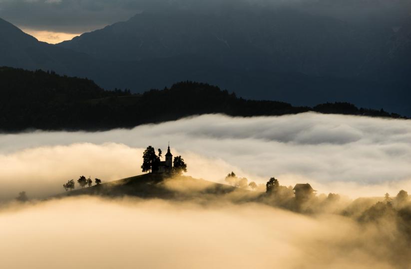 斯洛文尼亞共和國的山區層巒環繞，圖中一座山頂教堂在翻湧嫋繞的雲海間忽隱忽現...