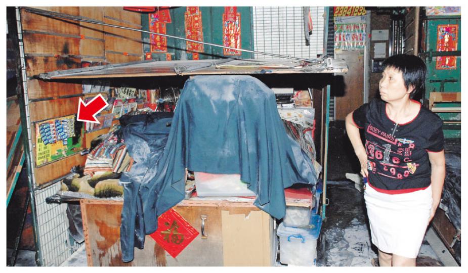 發生小火的路邊攤檔輕微損毁，一排掛在木板上的鈕形電池（箭嘴示）燒焦。女檔主事後趕返了解，一臉無奈。（李銘攝）