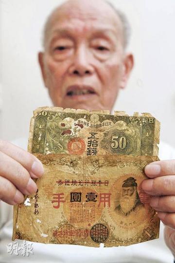 何國華手執兩張發黃穿洞的軍票,一張面值1元,一張5角。他說,當年4元港幣才值1元軍票,物價飛漲,經常要捱餓。(林振東攝) 何國華手執兩張發黃穿洞的軍票,一張面值1元,一張5角。他說,當年4元港幣才值1元軍票,物價飛漲,經常要捱餓。(林振東攝)