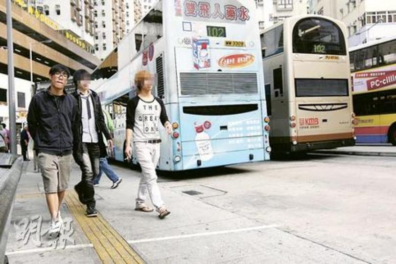 筲箕灣巴士總站僅在港鐵站出口旁邊劃了一條白線，煙民匆匆路過，隨時觸犯法例。圖中拿着香煙的市民（右及中）便位處禁煙區內。（郭慶輝攝）