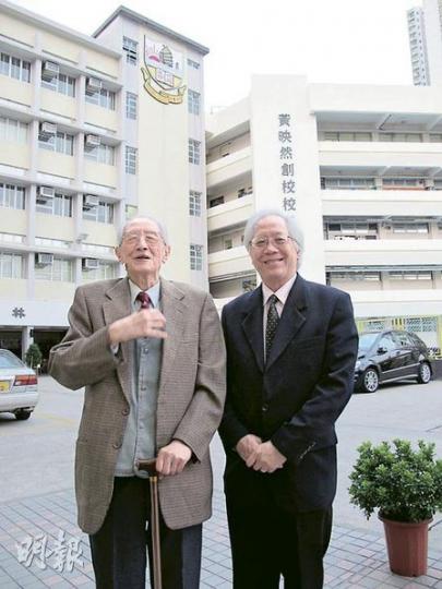 民生書院前任校監徐添福（左）及現任校監黃鉅鴻（右），口述民生書院歷史。背後大樓上的校徽位置，據說曾掛上英式大笨鐘，由於受舊啟德機場音頻影響，大笨鐘走慢30分鐘，令附近居民經常遲到還向學校投訴，最後傳聞被賣往南洋商場。（彭美芳攝）