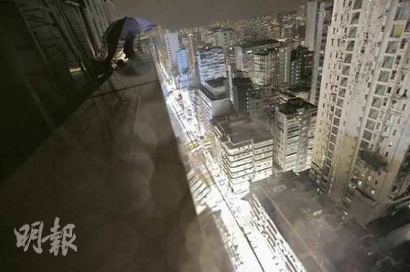 守於左上角傘下的便衣探員全天候在大廈天台監察街上情况，記者甫上天台便有探員即上前了解。 （何家達攝）