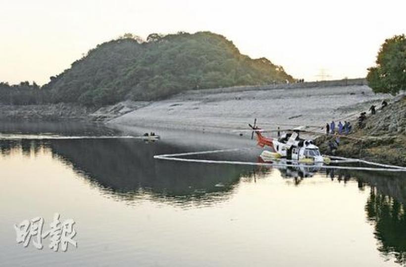 昨日事發期間，不少行山客停步在水壩上「觀賞」超級美洲豹落水及拯救過程（圖上方），至下午，水務署派員在附近圍起索油條，以防水源受污染（圖中白色帶）。肇事直升機預計要1至2日才能搬走，因水務署知會水塘水位未來24小時會下降約4吋，為免機身傾斜，工作人員昨晚在機艙再綁上4個藍色大膠桶防止入水下沉。（林振東攝）意外後，工程人員打開超級美洲豹的機頂引擎蓋檢查，初步調查後認為，直升機的右引擎出現故障，引致意外。（林振東攝）