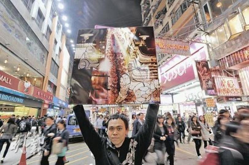 衛銘琛高舉經過加工的西洋菜街光污染相片，尤如外星人在大廈天台以死光掃射街上人群，以宣泄內心對光污染的不滿。（尹錦恩攝）