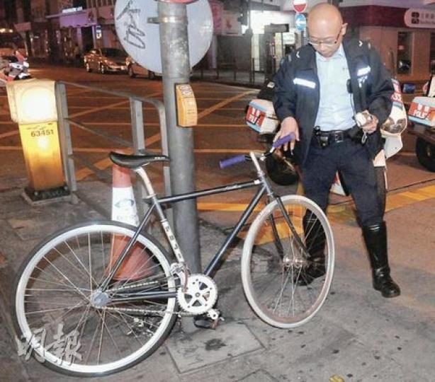 警員檢視肇事「梗牙單車」，該車前輪損毁，手把並無煞車掣。（蔡方山攝）騎「梗牙單車」涉嫌衝燈青年，遭的士撞傷送院治理。（蔡方山攝）