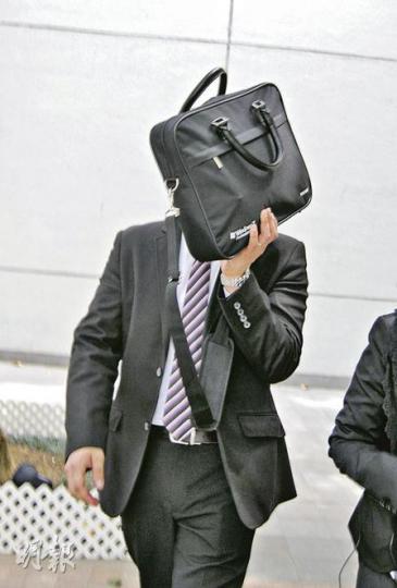 現役警員鍾志勇（以公文袋掩臉）昨在沙田裁判法院就盜竊罪受審。（梁珮珊攝）