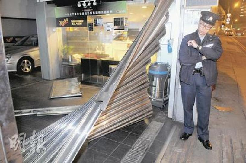 車房捲閘被撞後嚴重變形鬆脫，警員事後看守現場等候東主返回助查。（蔡方山攝）
