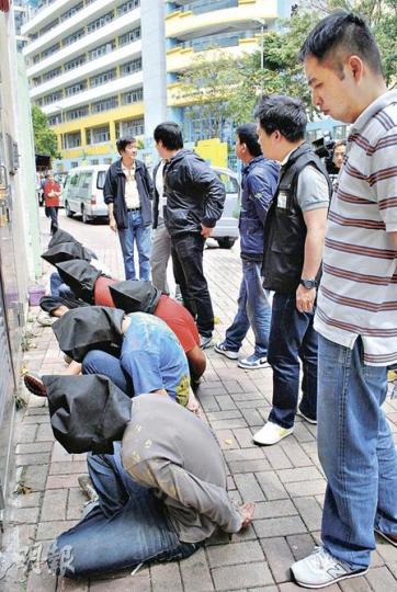 黑幫企圖壟斷秀茂坪區廢紙回收業，警方採取反黑行動打擊，涉案疑人黑布蒙頭面壁坐地等候帶署。（雲錦鋒攝）