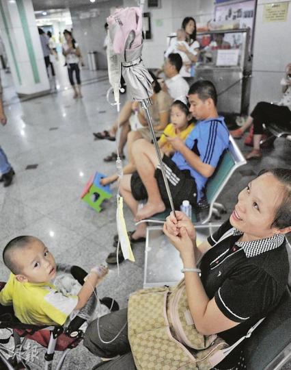 深圳市兒童醫院內坐滿了病人,3歲的小楊(左)發高燒,楊媽媽熟練地用雨傘當掛鈎,撑着藥水袋給孩子打點滴。(余俊亮攝) 深圳市兒童醫院內坐滿了病人,3歲的小楊(左)發高燒,楊媽媽熟練地用雨傘當掛鈎,撑着藥水袋給孩子打點滴。(余俊亮攝)