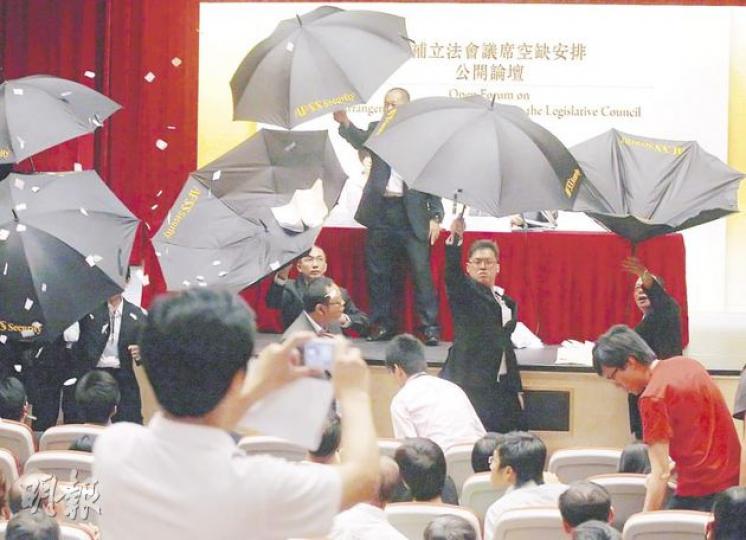 有出席論壇市民情緒激動,保安員早有準備,當有人向台上擲紙,便齊齊舉傘築起保護牆。(李紹昌攝)遞補機制首場公開論壇上,場面混亂,有示威者更將諮詢文件撕毁並擲向政制及內地事務局長林瑞麟(台上右方),幸得保安員舉傘保護,但保安員就被誤中副車。(李紹昌攝) 有出席論壇市民情緒激動,保安員早有準備,當有人向台上擲紙,便齊齊舉傘築起保護牆。(李紹昌攝)遞補機制首場公開論壇上,場面混亂,有示威者更將諮詢文件撕毁並擲向政制及內地事務局長林瑞麟(台上右方),幸得保安員舉傘保護,但保安員就被誤中副車。(李紹昌攝)