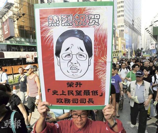 反對林瑞麟出任政務司長的遊行由銅鑼灣出發，有示威者高舉印有「熱烈祝賀」紙牌，諷刺林瑞麟在港大最近調查中得分只有38.5分，成為回歸以來民望最低的政務司長。（余俊亮攝）遊行者進入新政府總部旗杆空地後，公民黨、民主黨和人民力量等黨派，均展示印有其黨徽的橫額和直幡 ，但當民主黨拉起橫額時，一班人民力量成員隨即持直幡站在民主黨前，令畫面幾乎只見人民力量旗海。（余俊亮攝）