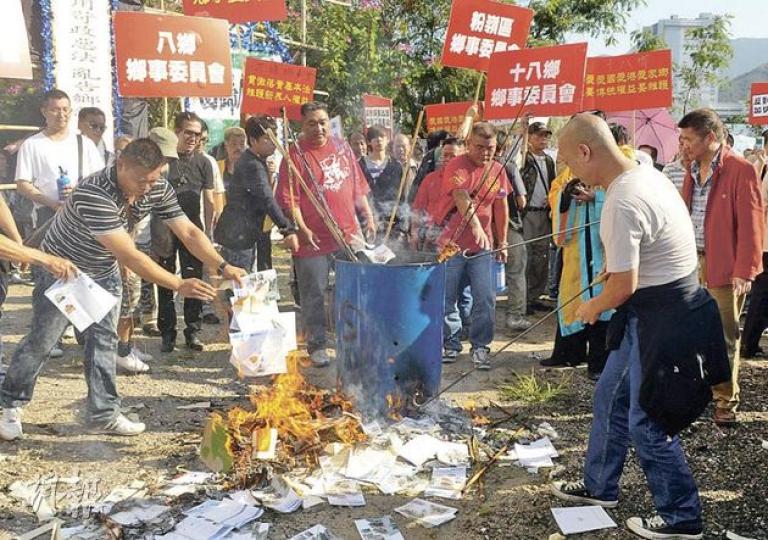 不滿政府執法對付僭建物的約千名新界原居民,昨午到鄉議局大樓門外抗議,搭建了「靈堂」布景及裝上「妖去民安」橫匾,並焚燒發展局長林鄭月娥的紙紮公仔及政府派發的清拆僭建物小冊子泄憤。(陳淑安攝)(明報製圖) 不滿政府執法對付僭建物的約千名新界原居民,昨午到鄉議局大樓門外抗議,搭建了「靈堂」布景及裝上「妖去民安」橫匾,並焚燒發展局長林鄭月娥的紙紮公仔及政府派發的清拆僭建物小冊子泄憤。(陳淑安攝)(明報製圖)