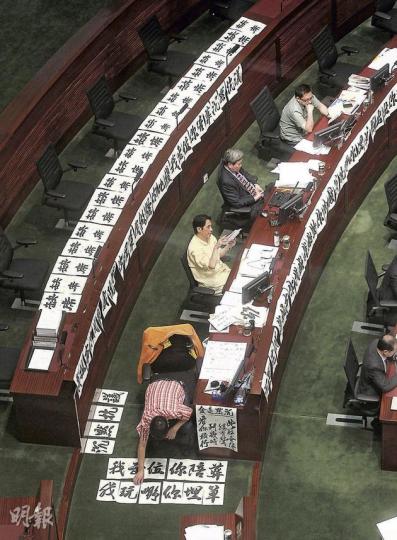 工聯會王國興（最前方面向地上）不甘人民力量的拉布戰，逕自寫毛筆字、貼大字報發泄，「沉默抗議」、「你拉布我埋單」、「我出位你陪葬」、「缺席」等字句，至晚上有關大字已貼滿王國興座位前後三排。左二起為黃國健、潘佩璆、葉偉明。（李澤彤攝） 拉布戰主要靠人民力量黃毓民（左）、陳偉業（右）及社民連主席梁國雄出招，剛於上周完成白內障及眼角膜手術的黃毓民，昨偶爾要滴眼藥水。（李澤彤攝） 朝九晚十的會議，政制及內地事務局長譚志源不顧鏡頭也要站起來拉拉筋，以打這場持久戰。（李澤彤攝）