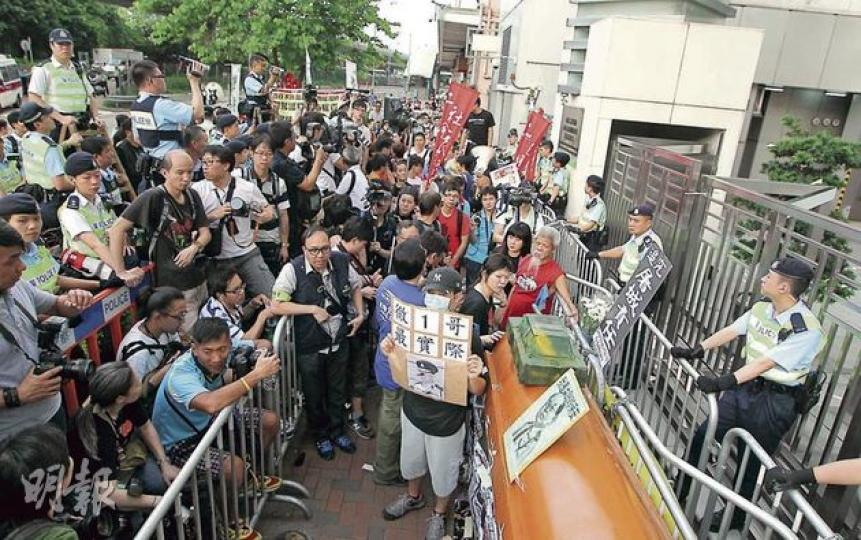 遊行隊伍到達中聯辦後，將棺材、紙坦克等示威物品放在門外，警員以兩重鐵馬隔開示威者與中聯辦，並有警員手持攝影機記錄示威情况。（李澤彤攝） 有示威者在中聯辦門外展示畫上交叉的警務處長曾偉雄的相片，以示不滿。（余俊亮攝）