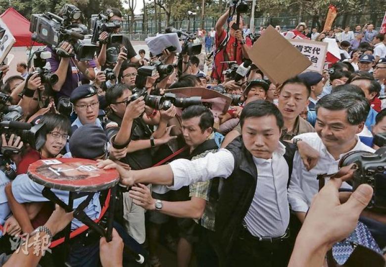 特首梁振英(前排右一)昨日到黃大仙時需警方開路才可進入會場,原本他計劃到請願區接信,但最終由警方護送下直接入會場。社民連將貼上梁振英肖像和寫有「下台」兩字的摺櫈遞到梁振英面前,隨即被G4擋開。(李澤彤攝) 特首梁振英(前排右一)昨日到黃大仙時需警方開路才可進入會場,原本他計劃到請願區接信,但最終由警方護送下直接入會場。社民連將貼上梁振英肖像和寫有「下台」兩字的摺櫈遞到梁振英面前,隨即被G4擋開。(李澤彤攝)