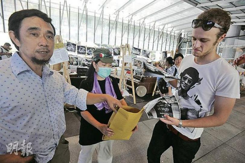 意大利遊客(右)想購買原本僅作展覽用途的香港街頭照片,被告何耀勝(左)和另一參加者譚小姐(中)即場收取300元賣出3張照片,又聲稱獲授權賣相籌款,但相片策展人否認有賣相安排。(尹錦恩攝) 意大利遊客(右)想購買原本僅作展覽用途的香港街頭照片,被告何耀勝(左)和另一參加者譚小姐(中)即場收取300元賣出3張照片,又聲稱獲授權賣相籌款,但相片策展人否認有賣相安排。(尹錦恩攝)