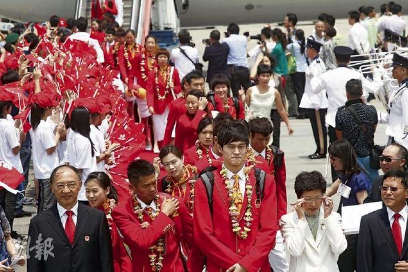 奧運金牌運動員昨抵港，在團長、國體總局長劉鵬（前排左一）帶領下步出停機坪，帶頭的運動員是奧運游泳兩金得主孫楊（前排右二），政務司長林鄭月娥（前排右二）到場接機，在酷熱天氣下舉行迎接儀式。（李紹昌攝） 代表團舉行的記者會上，運動員多次被記者問及有關國民教育的問題，台上的孫楊及吳敏霞不知就裏，不時互相對望，用笑容向對方「求救」。（李紹昌攝） 在倫奧因0.1分失全能「吊環王」陳一冰（中），在港首晚便在化妝品店大有收穫，離開時有保安員為他開路。（梁榮達攝） 中國金牌游泳運動員孫楊（中）昨日逛電器連鎖店時