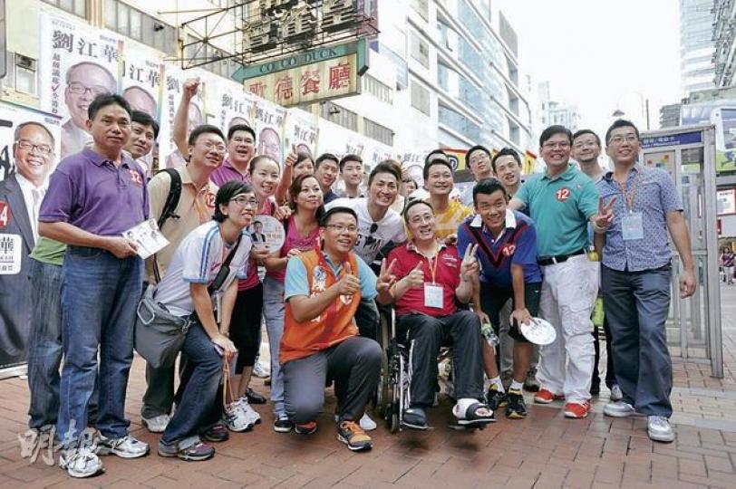 民建聯新界西候選人陳恒鑌（前排橙衣者）於荃灣和其支持者合照，香港乒乓球代表隊成員唐鵬和帖雅娜及藝人何家勁到場支持。（葉家豪攝） 