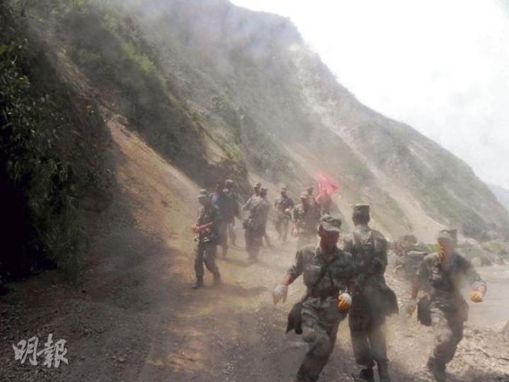 記者進入震央半路突然有落石，現場沙塵四起，救援人員奔走躲避。（李泉攝） 昨日災區開始有死者出殯。圖為親屬在場等待送殯。（李泉攝） 震央洛澤河鎮中心街頭，除了落石和救援人員，街上一片冷清。（李泉攝）