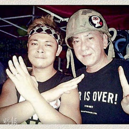黃秋生（右）戴着貼有反洗腦貼紙的頭盔，與梁祖堯到政總的公民廣場以示支持。（微博圖片）