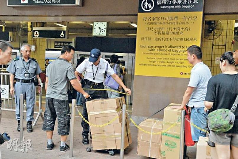 上水港鐵站職員昨日在站外逐一量度水貨客的大型行李。（伍浦鋒攝） 警方昨日在上水港鐵站附近實施人流管制行政措施，圖為水貨客於站外排隊。（伍浦鋒攝）