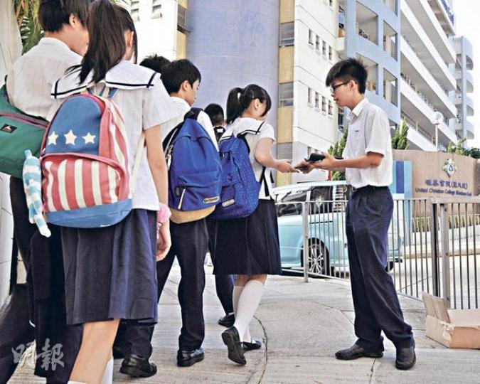 學民思潮召集人黃之鋒（右）昨日在上課前，於校門外向同學派發反洗腦小冊子，希望他們可更清楚國教科的問題。（葉家豪攝）（明報製圖）