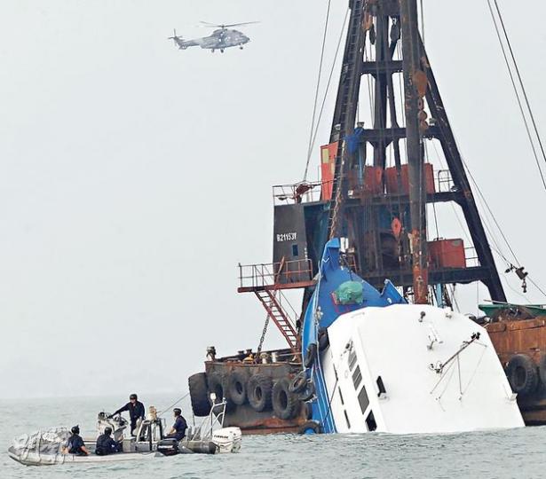 港燈客船「南丫四號」事發後一直由躉船懸吊，一半船身傾斜沒入海中，水警駕駛橡皮艇在躉船附近巡邏，直升機亦一直在上空盤旋。客船至昨下午被撈起。（李紹昌攝）
