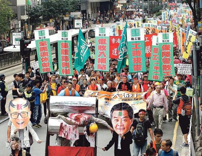 職工盟昨發起五一大遊行,遊行主題為「公平、尊嚴、家庭友善」,由正在罷工的碼頭工人打頭陣。他們在象徵官商壓榨工人的「人肉榨汁機」「帶領」下,由維園遊行至政府總部及長江中心,再前往和記大廈抗議。(李紹昌攝) 職工盟昨發起五一大遊行,遊行主題為「公平、尊嚴、家庭友善」,由正在罷工的碼頭工人打頭陣。他們在象徵官商壓榨工人的「人肉榨汁機」「帶領」下,由維園遊行至政府總部及長江中心,再前往和記大廈抗議。(李紹昌攝)
