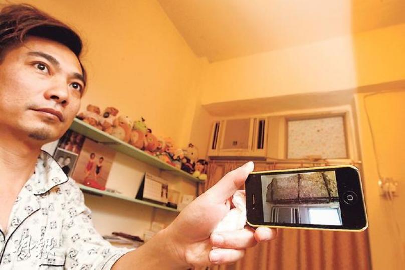 住在西環新安大廈7樓的許先生，月前家中冷氣機對上的一幅石屎牆突然倒塌（見圖中iPhone屏幕），他質疑這與港鐵工程有關，但由於擔心調查需時，最終選擇自行維修。（李紹昌攝）