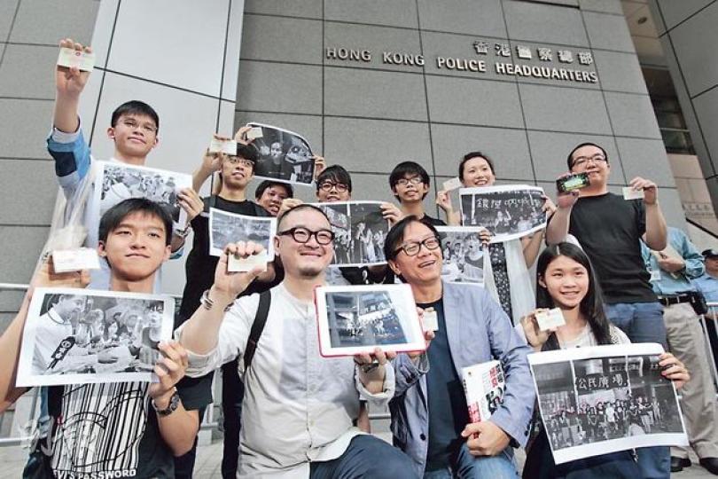 警方事隔22個月拘捕佔中義工陳玉峰，並說已通緝陳多時，引發11名去年反國民教育科集會人士，包括張秀賢（前排左起）、邵家臻、韓連山、黃莉莉等昨日帶同參與反國教科的照片，到警察總部「投案」，查詢自己是否在低調通緝的名單上。圖後排左起為黎汶洛、陳樹暉、蕭超杰、林朗彥、黃之鋒、葉寶琳及陳景輝。（郭慶輝攝）11名反國教科集會核心成員昨日事先張揚「投案」，警方如臨大敵，在灣仔警察總部外佈滿鐵馬，每個門口均有多名軍裝警員把守，多名警長亦在場監視。（郭慶輝攝）