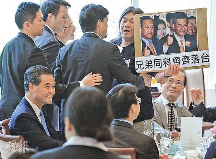 社民連梁國雄(右一、站立者)高舉印有梁振英同前行會成員張震遠相片嘅標語,批評梁張「一擔擔」,冇資格做特首,但梁振英(左一、坐下者)望都唔望,繼續微笑。(劉焌陶攝) 社民連梁國雄(右一、站立者)高舉印有梁振英同前行會成員張震遠相片嘅標語,批評梁張「一擔擔」,冇資格做特首,但梁振英(左一、坐下者)望都唔望,繼續微笑。(劉焌陶攝)