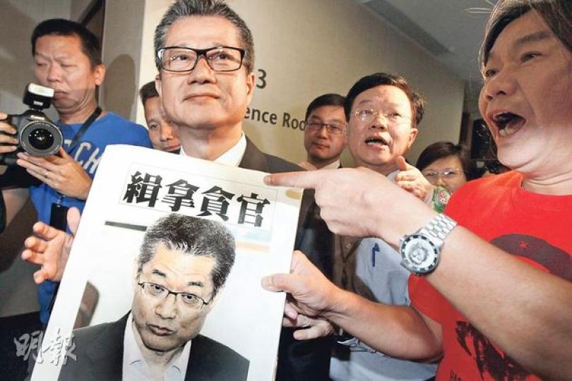 發展局長陳茂波（前左）昨到立法會出席發展事務委員會特別會議時，社民連立法會議員梁國雄（右）向他遞上「緝拿貪官」的海報，要他下台。（李紹昌攝）