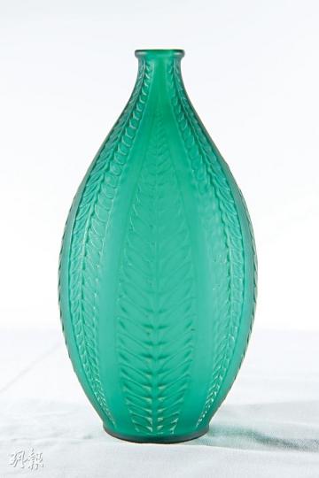 Acacia花瓶（1921年作品）﹕少有鮮色的René Lalique玻璃作品，1947年停產，直至近年才重新推出，但已改為清水晶及紅水晶（分別售$7300及$8500）。Acacia瓶身是金合歡樹的樹葉圖案，金合歡樹象徵生命不朽和神秘知識。李少傑1990年代在巴黎購入，當時購入價約為20萬港元。（黃志東攝）Lalique香水瓶Petites feuilles（1910作品）﹕René Lalique於1905年首先為COTY設計香水瓶。李少傑認為，要收藏Lalique便一定要有一件香水瓶，因為