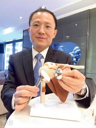 骨科專科醫生周啟斌表示,本港近年引入「反向肩關節置換術」, 病人可借助肩膀肌肉拉動手臂,筋腱受損者亦可恢復活動能力。(梁杏怡攝)現年80歲的雷婆婆(右)向來身體壯健,2011年到西班牙旅遊時不慎摔倒,令右肩關節及手骨骨折,回港後確認肩關節碎裂嚴重,不適合做傳統手術,選擇做「反向肩關節置換手術」,置換了人工肩關節後,已可如常舉起雙手,左為其主診醫生周啟斌。(梁杏怡攝) 骨科專科醫生周啟斌表示,本港近年引入「反向肩關節置換術」, 病人可借助肩膀肌肉拉動手臂,筋腱受損者亦可恢復活動能力。(梁杏怡攝)現年80歲的雷婆婆(右)向來身體壯健,2011年到西班牙旅遊時不慎摔倒,令右肩關節及手骨骨折,回港後確認肩關節碎裂嚴重,不適合做傳統手術,選擇做「反向肩關節置換手術」,置換了人工肩關節後,已可如常舉起雙手,左為其主診醫生周啟斌。(梁杏怡攝)
