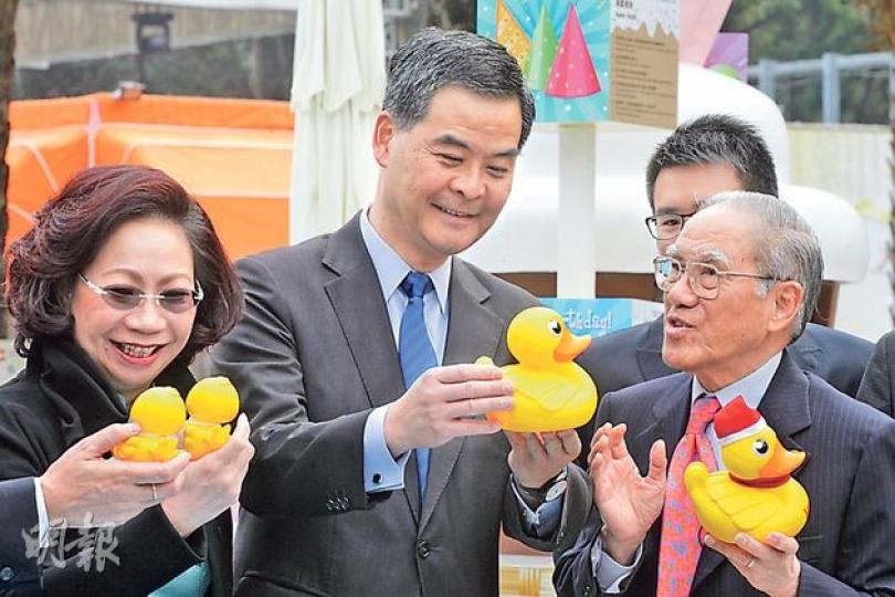 行會成員林健鋒的父親林亮(右)在工展會攤檔,為梁振英伉儷介紹「工展鴨」,梁振英(中)即以約4900元掃貨,買入大批工展鴨文件夾及杯蓋,其妻唐青儀(左)昨在另一活動把工展鴨物品轉送給一班小朋友。(李紹昌攝) 行會成員林健鋒的父親林亮(右)在工展會攤檔,為梁振英伉儷介紹「工展鴨」,梁振英(中)即以約4900元掃貨,買入大批工展鴨文件夾及杯蓋,其妻唐青儀(左)昨在另一活動把工展鴨物品轉送給一班小朋友。(李紹昌攝)
