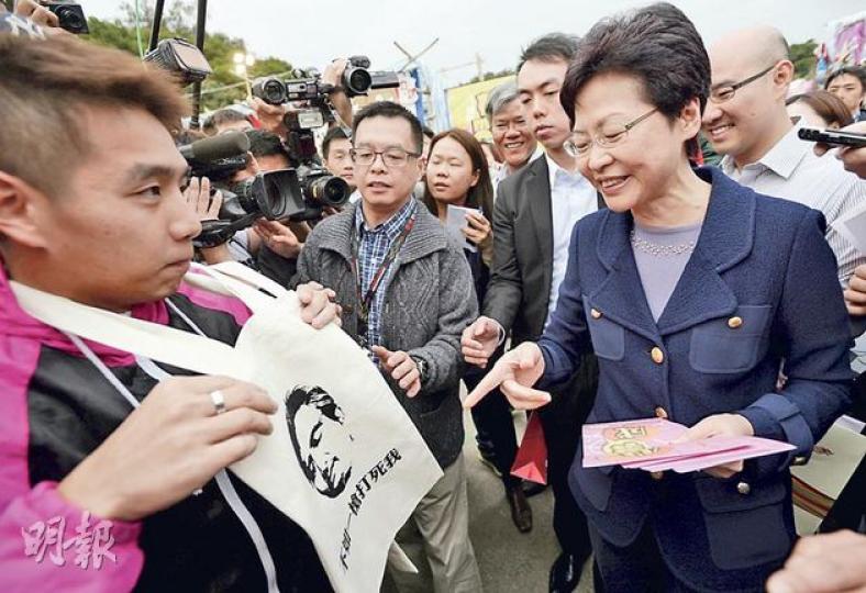 政務司長林鄭月娥(右)昨日到旺角界限街花墟公園參觀年宵巿場,一名青年(圖)頸上掛着一個印有「不如一槍打死我」字樣的布袋,向林鄭月娥示威,並高呼「不要假諮詢,只要真普選」。林鄭月娥面帶笑容指着圖樣,但未有正面回應。(余俊亮攝) 政務司長林鄭月娥(右)昨日到旺角界限街花墟公園參觀年宵巿場,一名青年(圖)頸上掛着一個印有「不如一槍打死我」字樣的布袋,向林鄭月娥示威,並高呼「不要假諮詢,只要真普選」。林鄭月娥面帶笑容指着圖樣,但未有正面回應。(余俊亮攝)