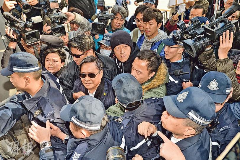 黃毓民（圖中墨鏡西裝者）昨到庭時遭大批示威者辱罵：「黃毓民坐監！」及「黃毓民快啲死！」，黃則表現從容，面帶微笑，在其支持者及警方護送下進入法庭。（鄧宗弘攝）
