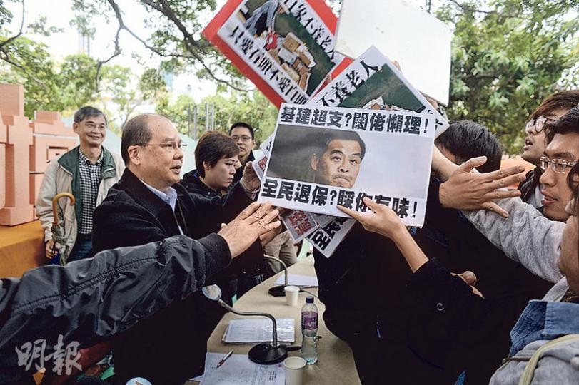 昨日論壇完結時有民主黨和社民連成員手持標語牌衝向台前,要求勞福局長張建宗(左)接請願信,推行不設審查的全民退保,張建宗最後要由工作人員「開路」上車離開。勞福局發言人說,張建宗原準備「企定定」與其對話,但因現場保安安排離開,他最後接過3封請願信。(鍾林枝攝) 昨日論壇完結時有民主黨和社民連成員手持標語牌衝向台前,要求勞福局長張建宗(左)接請願信,推行不設審查的全民退保,張建宗最後要由工作人員「開路」上車離開。勞福局發言人說,張建宗原準備「企定定」與其對話,但因現場保安安排離開,他最後接過3封請願信。(鍾林枝攝)