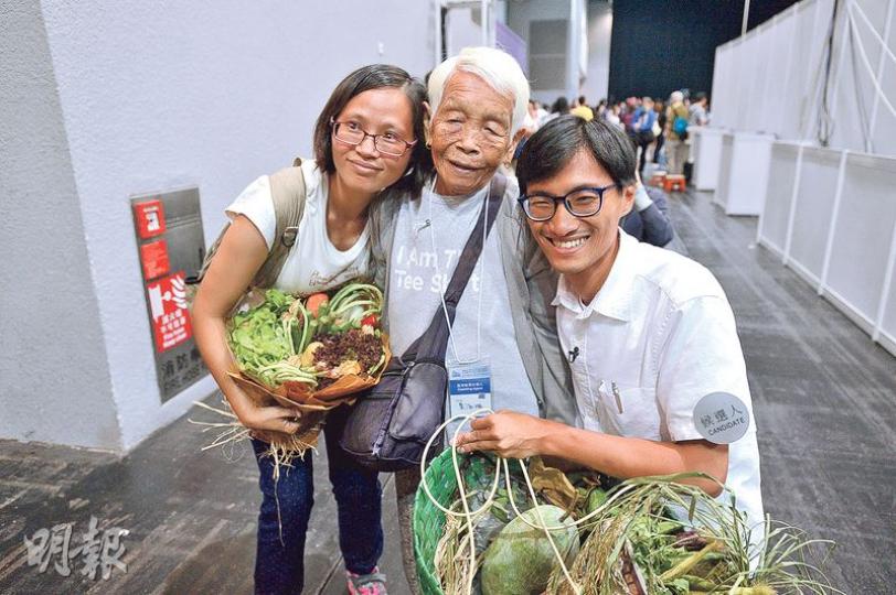 朱凱廸（右）一直推動「民主自決，城鄉共生」，當年有份參與反對清拆菜園村運動，與村民關係深厚。89歲菜園村村民高婆婆（中）昨早4時起牀，乘的士到點票中心撐場，當知道朱凱廸獲得逾8萬票時表現雀躍，大呼「我好開心呀」，並送了一籃自家種蔬菜給他。左為朱凱廸妻子。（鍾林枝攝）