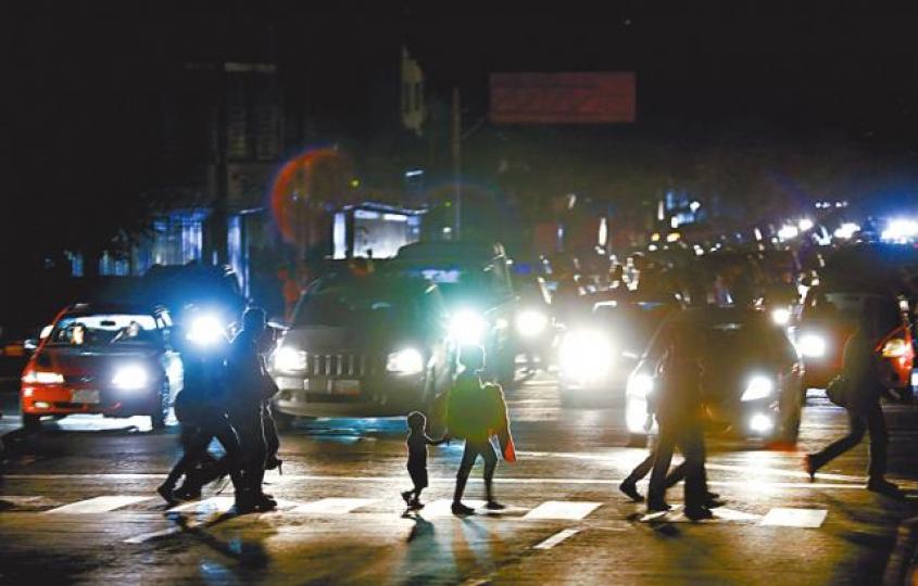 停電沒路燈下，卡拉卡斯市民摸黑在車頭燈光中過馬路。　美聯社