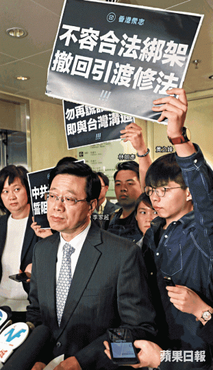 保安局長李家超昨為修訂《逃犯條例》解畫,香港眾志秘書長黃之鋒等人在後方高舉示威標語。謝榮耀攝 保安局長李家超昨為修訂《逃犯條例》解畫,香港眾志秘書長黃之鋒等人在後方高舉示威標語。謝榮耀攝
